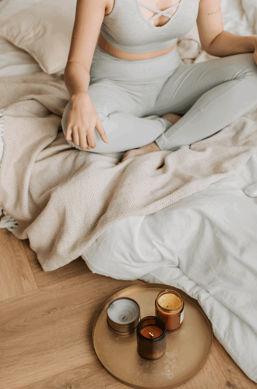Femme en tenue confortable méditant sur un lit avec des bougies allumées, illustrant la gestion des émotions et des fringales pendant le cycle menstruel